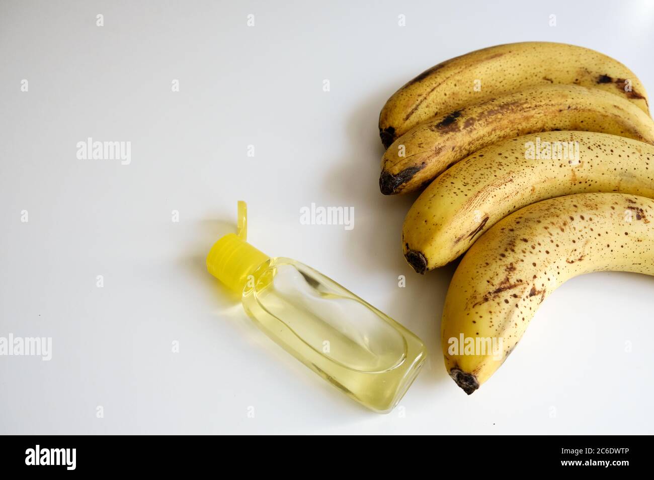 Vista ravvicinata di una fila di banane gialle e di una bottiglia di igienizzatore a mano su una scrivania bianca. Dieta sana per una buona immunità e diffusione del virus covid-19 Foto Stock