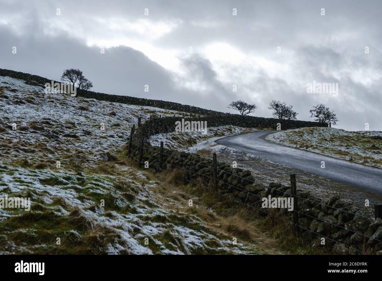 Una strada fredda e desolata vicino alla montagna di Slemish in Co. Antrim, Irlanda del Nord con leggera polvere di neve nei campi e minacciando cieli grigi Foto Stock