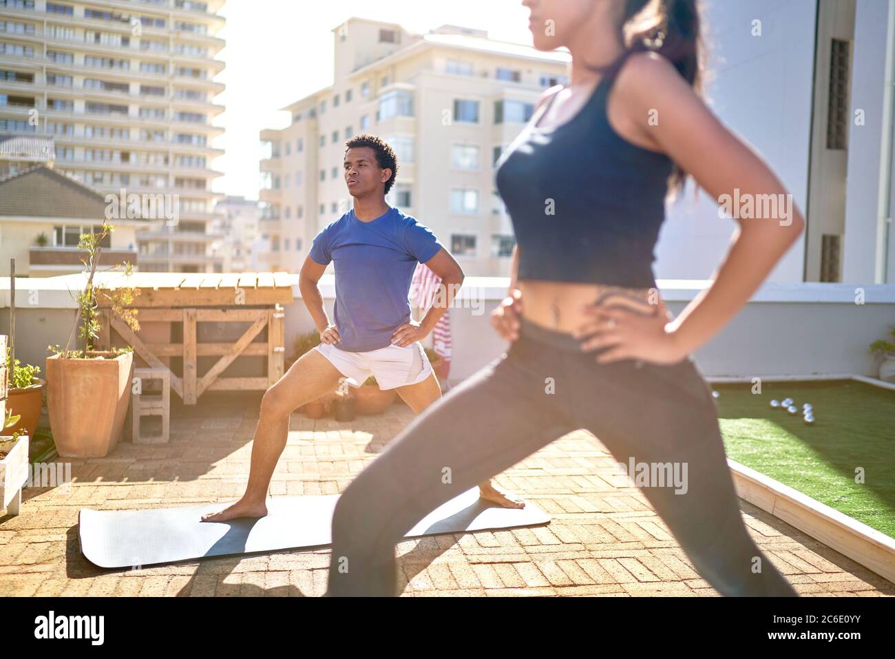 Giovane coppia che pratica yoga sul soleggiato tetto urbano Foto Stock