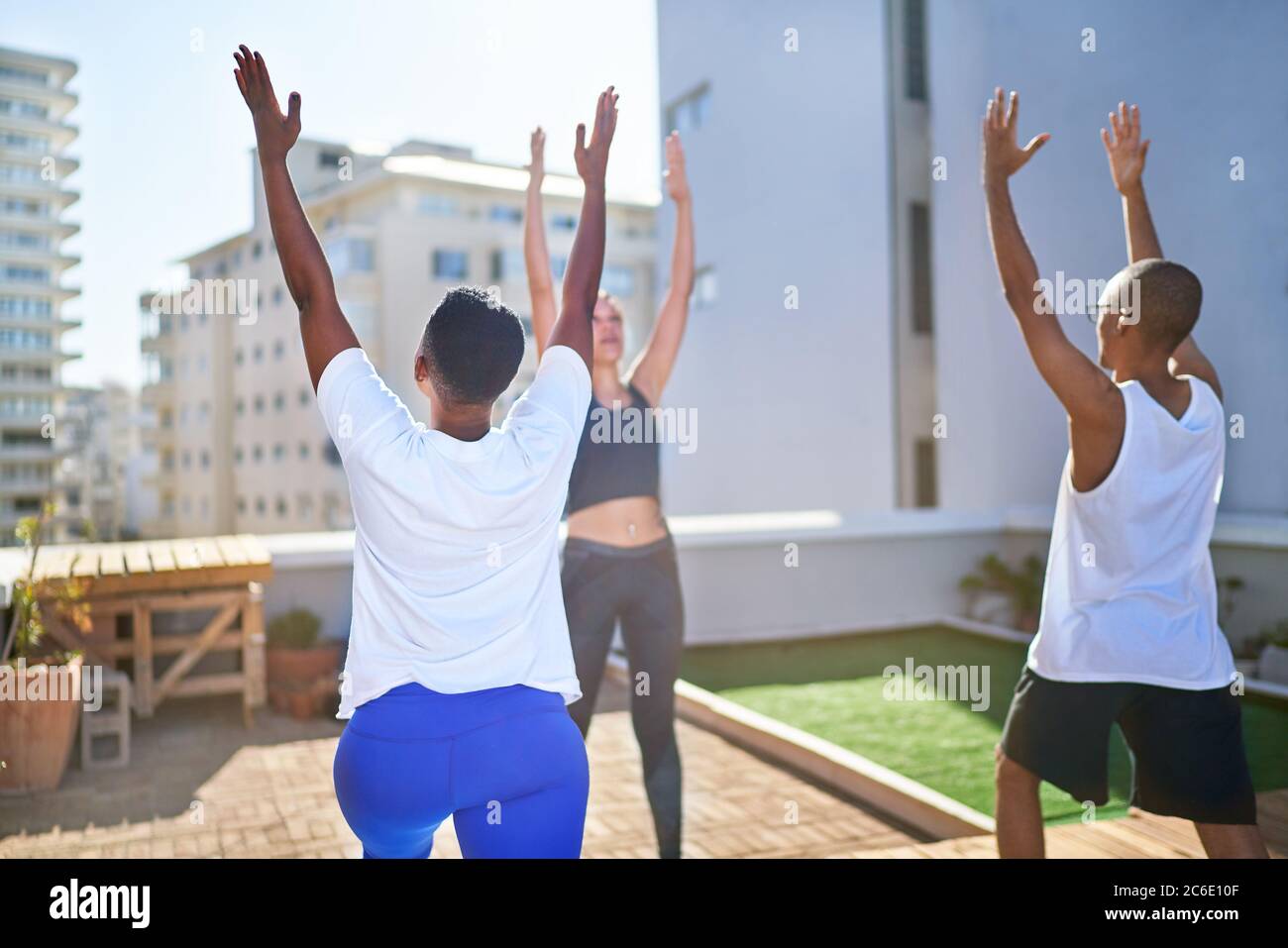 Amici che praticano yoga sul soleggiato tetto urbano Foto Stock