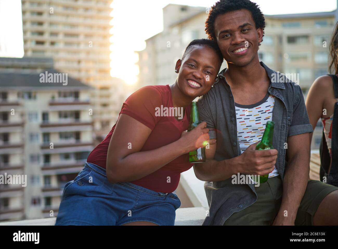 Ritratto felice giovane coppia bevendo birra sul tetto urbano Foto Stock