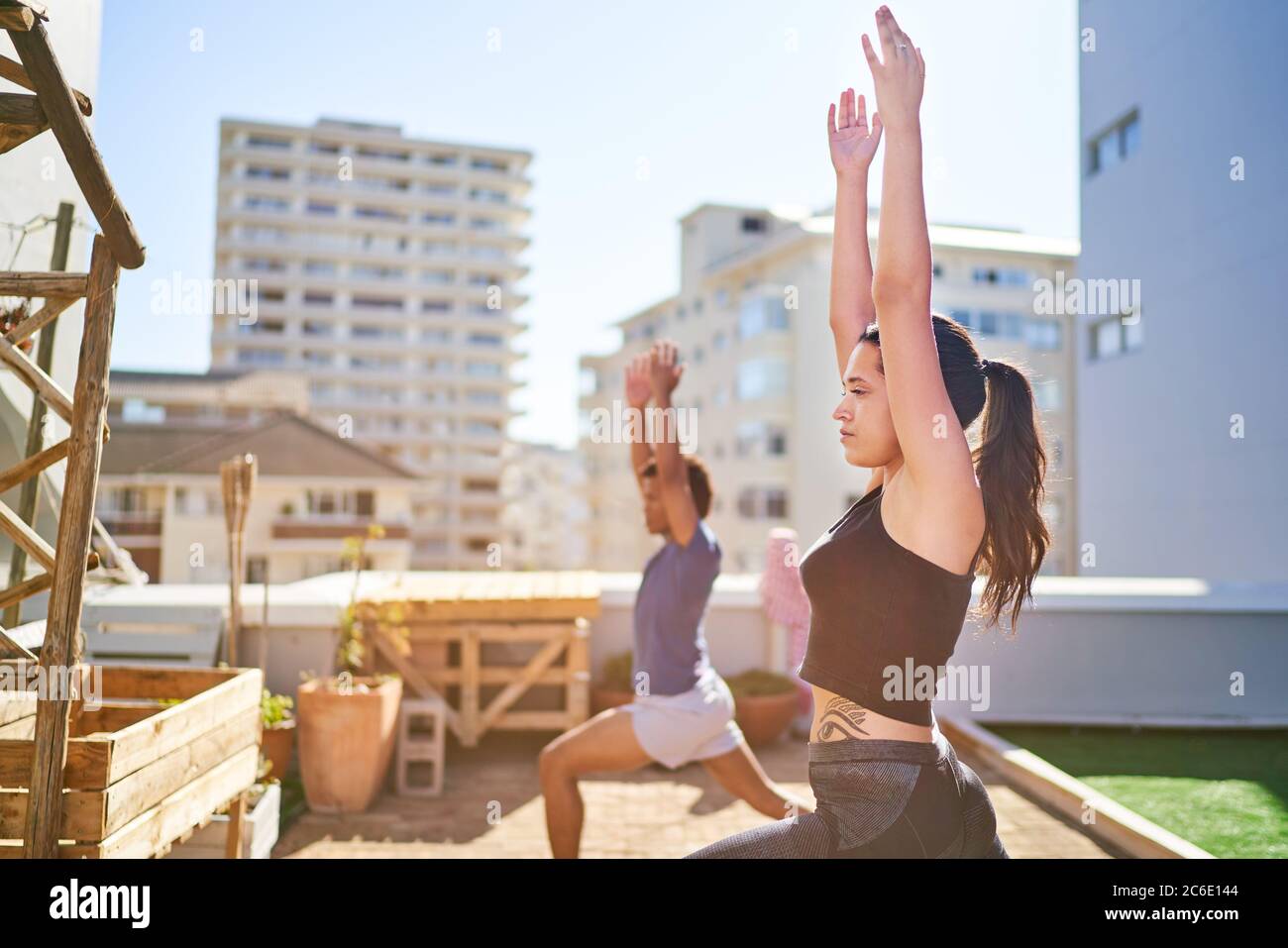 Giovane uomo e donna che pratica yoga sul soleggiato tetto urbano Foto Stock