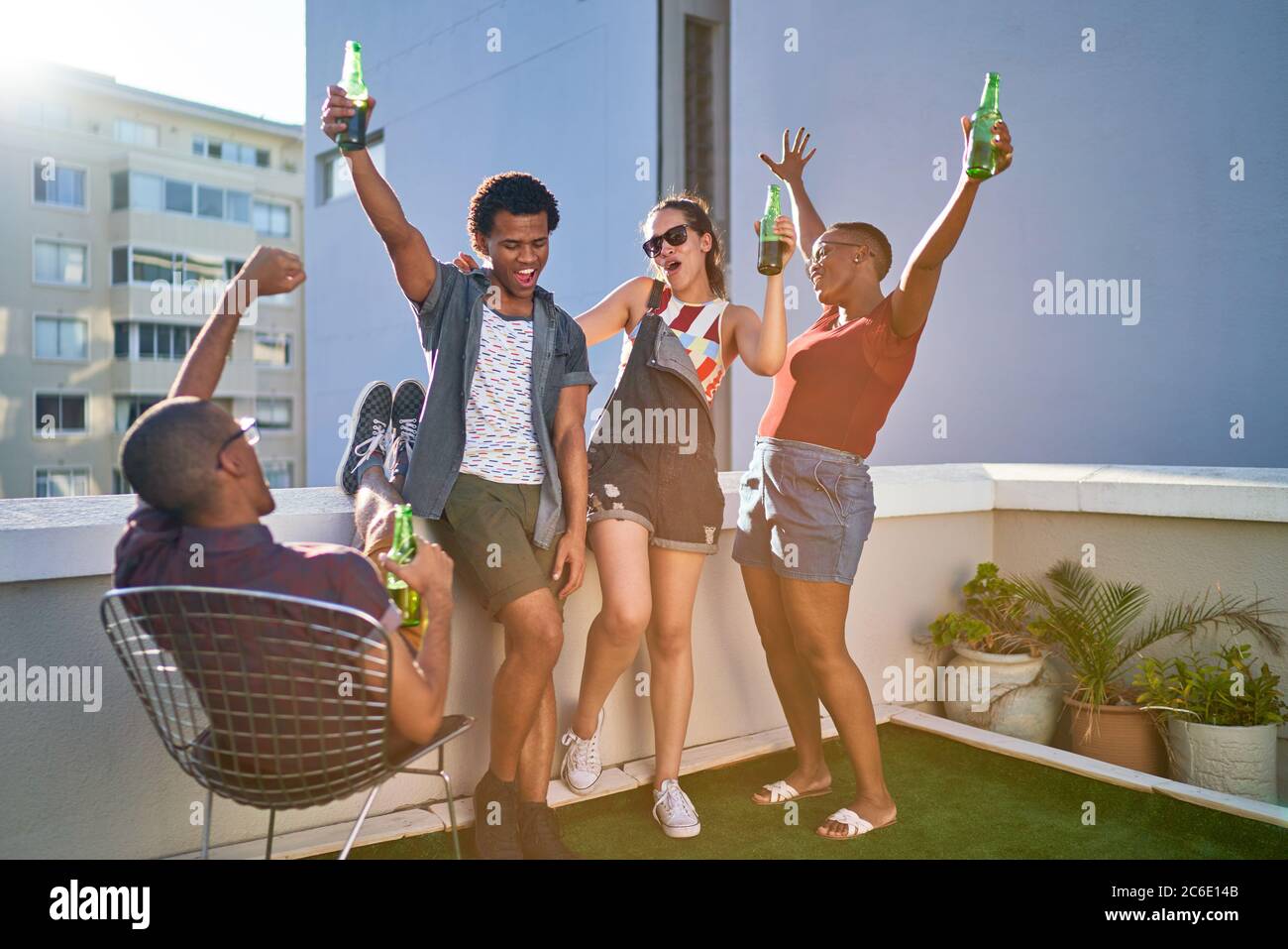 Felici i giovani amici che si acclamano e bevono birra sul tetto urbano Foto Stock