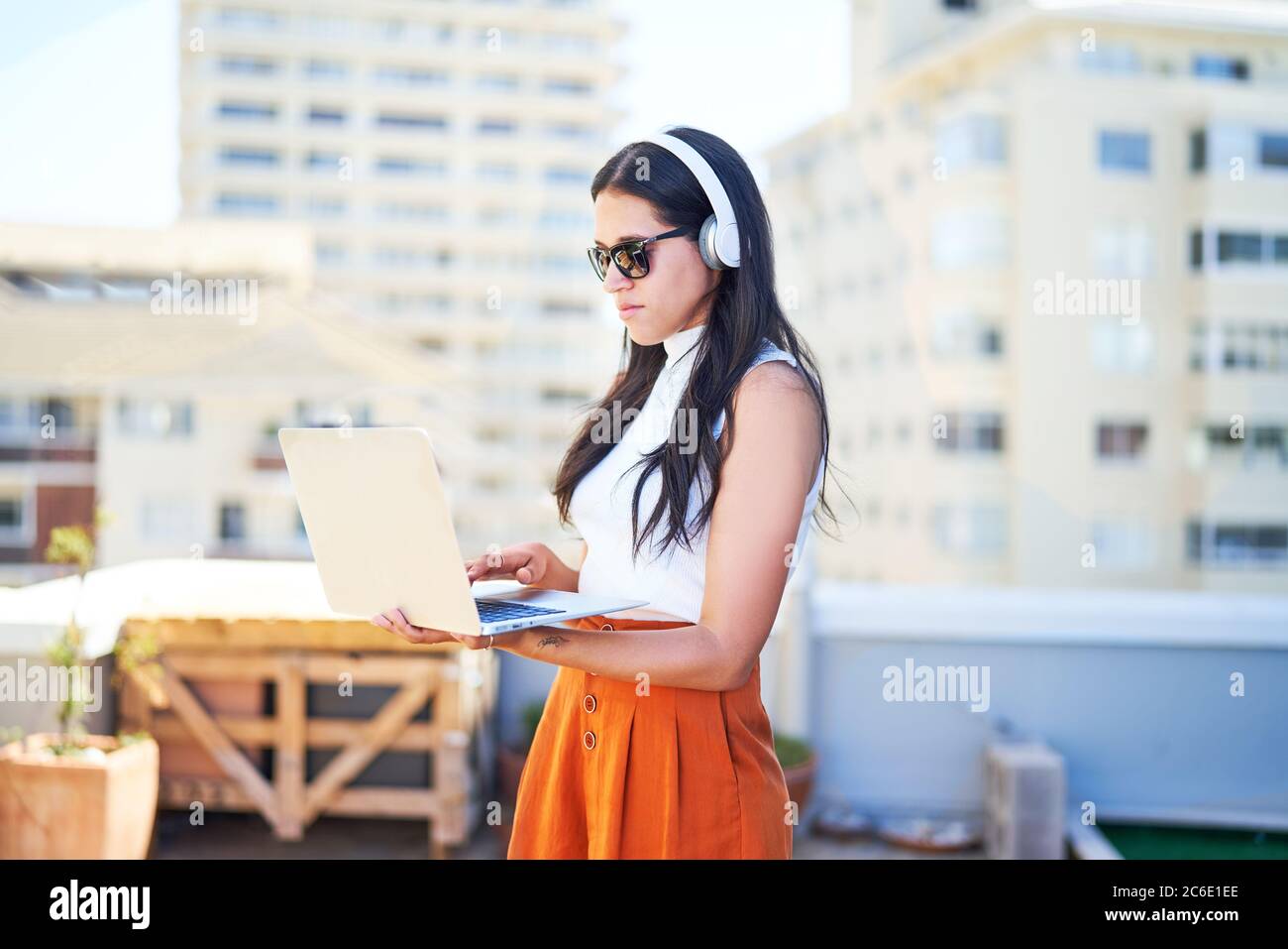 Giovane donna con cuffie e computer portatile che lavora sul tetto urbano Foto Stock