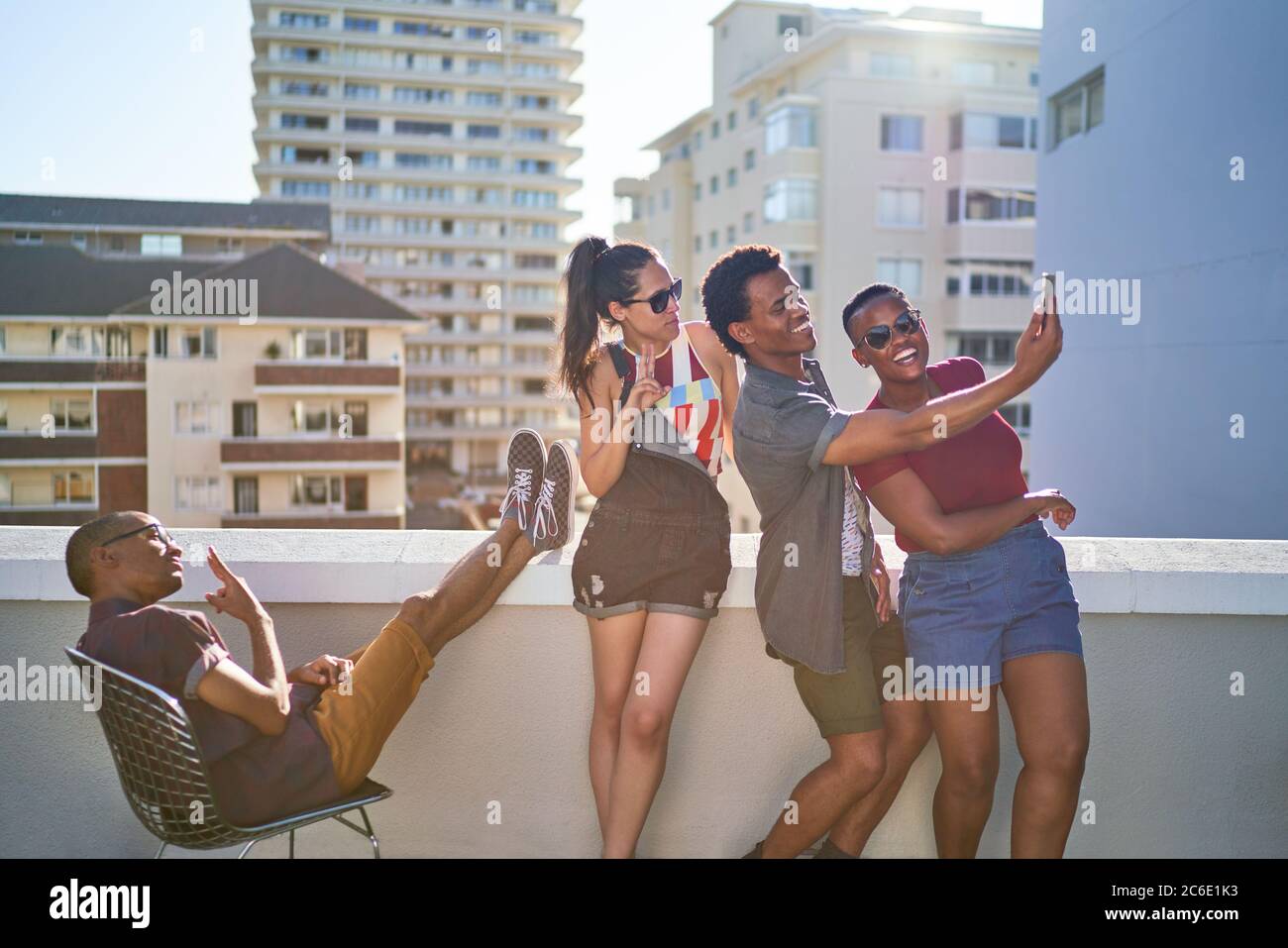 Felici i giovani amici che prendono selfie sul tetto della soleggiata terrazza urbana Foto Stock