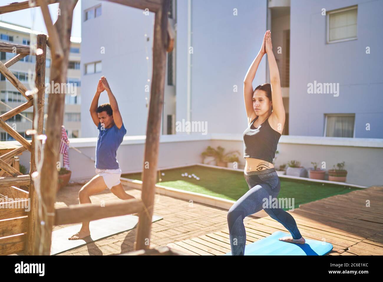 Giovani amici che praticano yoga sul soleggiato tetto urbano Foto Stock
