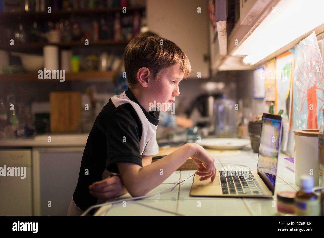 Ragazzo che fa i compiti a un computer portatile sul banco della cucina Foto Stock