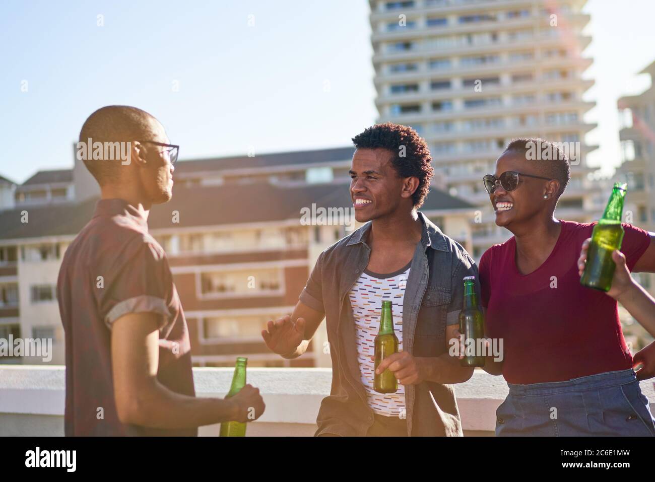 I giovani amici parlano e bevono birra sul soleggiato balcone urbano sul tetto Foto Stock
