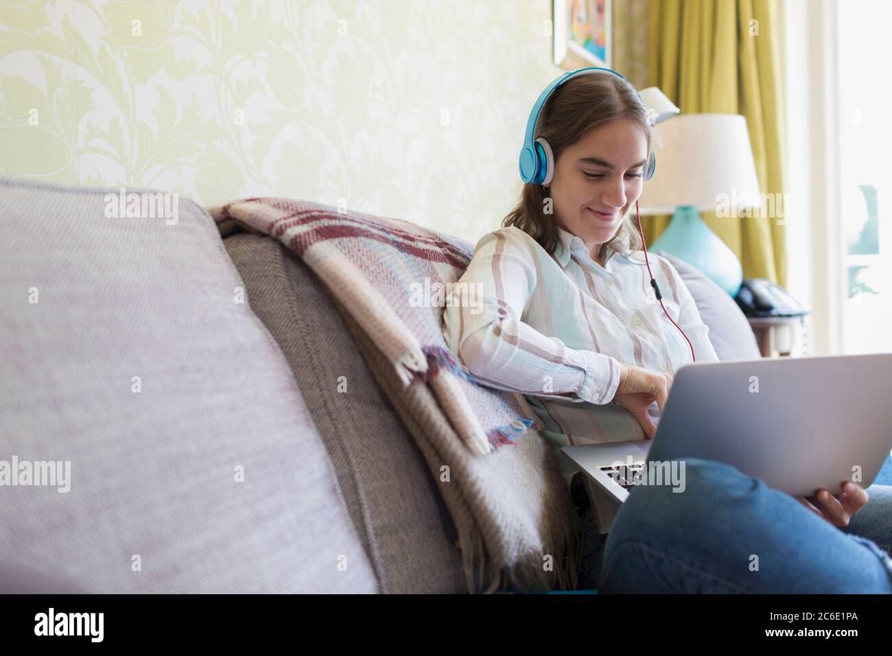 Ragazza adolescente con cuffie che usano il computer portatile sul divano Foto Stock