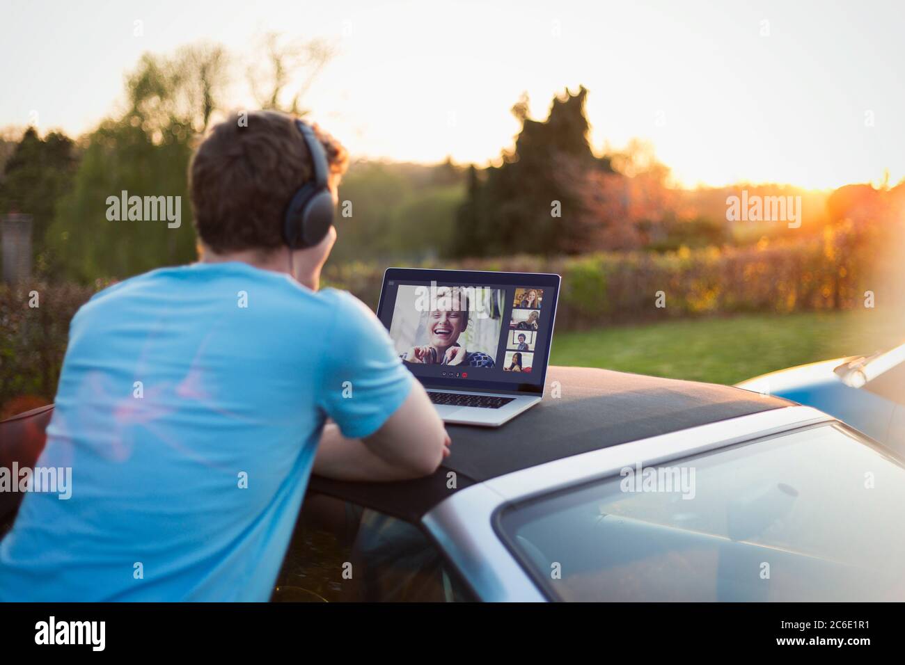 Uomo con cuffie e laptop che parla con gli amici sul tetto dell'auto Foto Stock