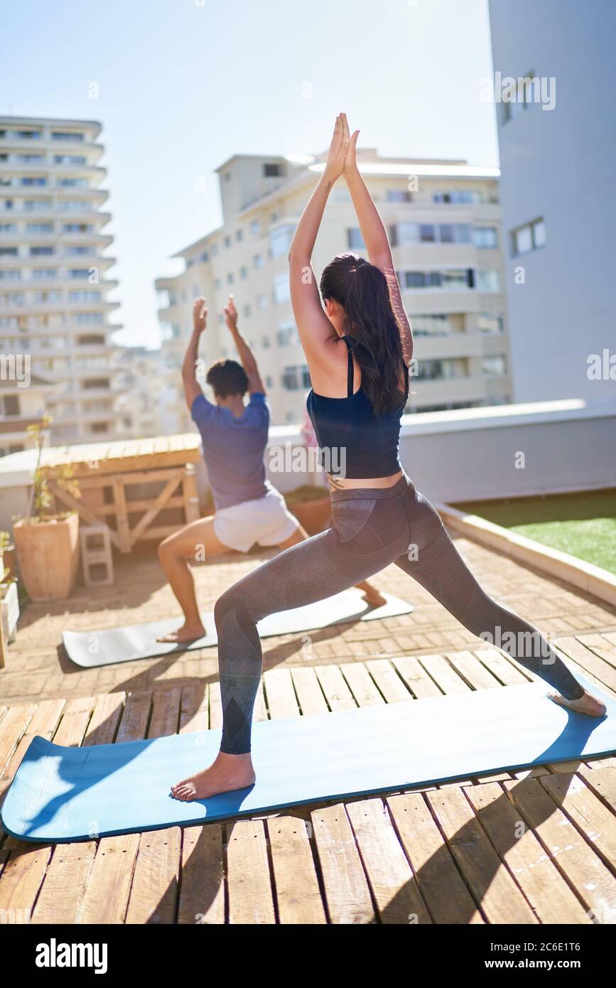Giovane coppia che pratica yoga sul soleggiato balcone urbano sul tetto Foto Stock