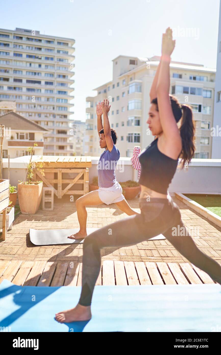Giovane coppia che pratica yoga sul soleggiato balcone urbano sul tetto Foto Stock