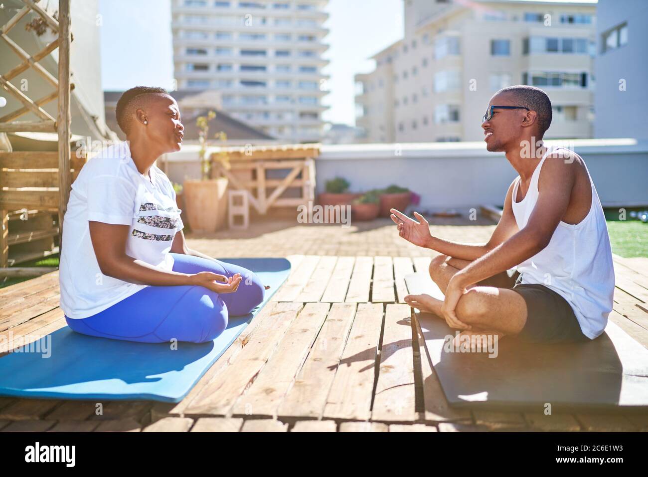 Giovane coppia che parla di stuoie yoga sul soleggiato balcone urbano sul tetto Foto Stock