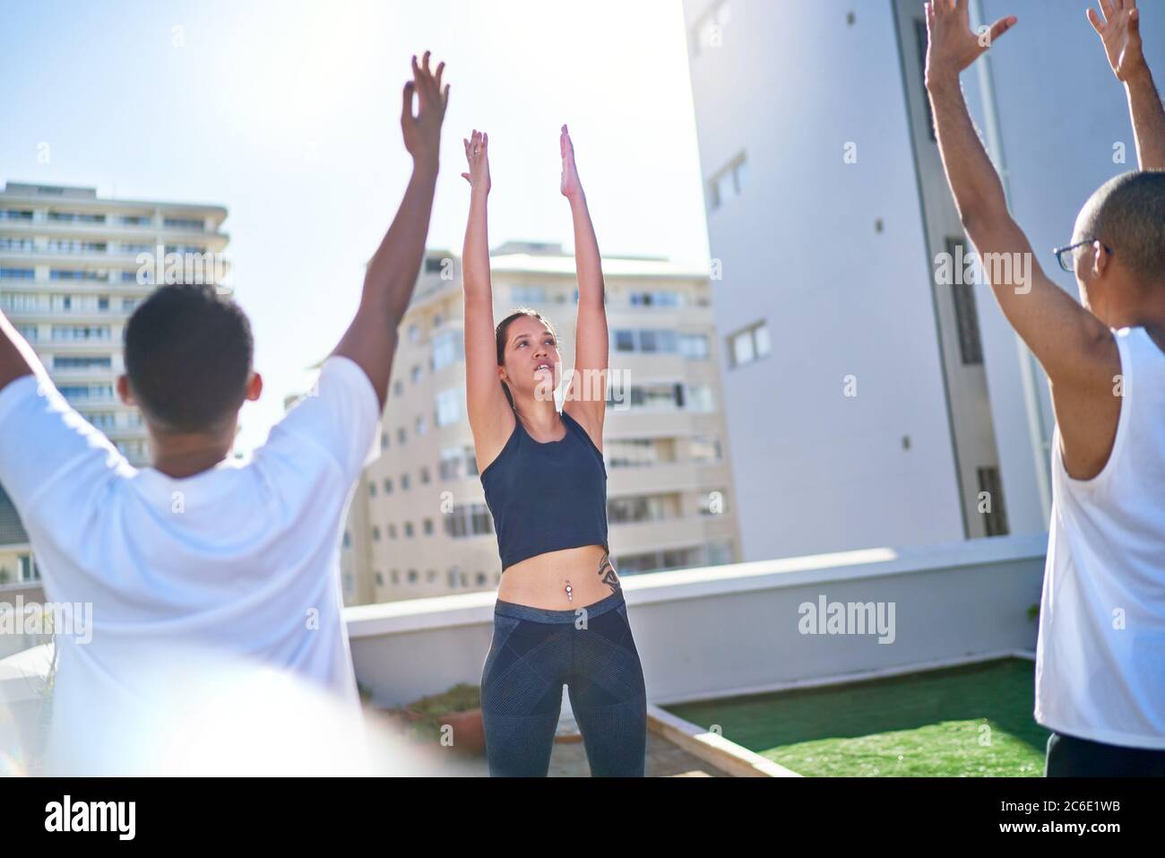 Giovani amici che praticano yoga sul soleggiato balcone urbano sul tetto Foto Stock