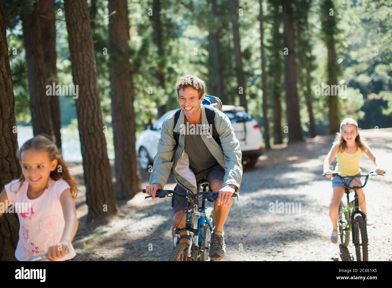 Sorridente padre e figlie in bicicletta a cavallo in boschi Foto Stock