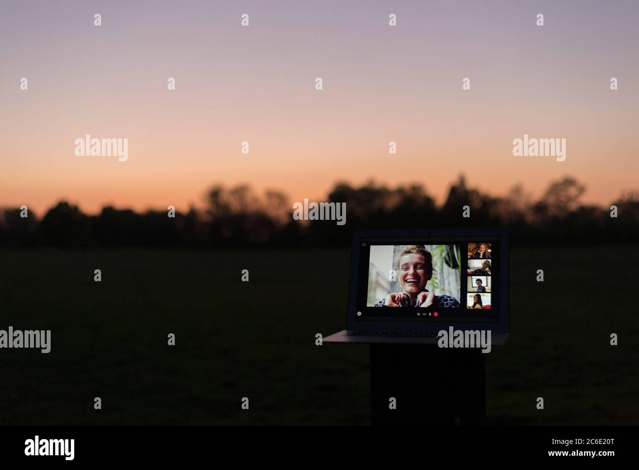 Amici che videochattano sullo schermo del laptop nel parco al tramonto Foto Stock