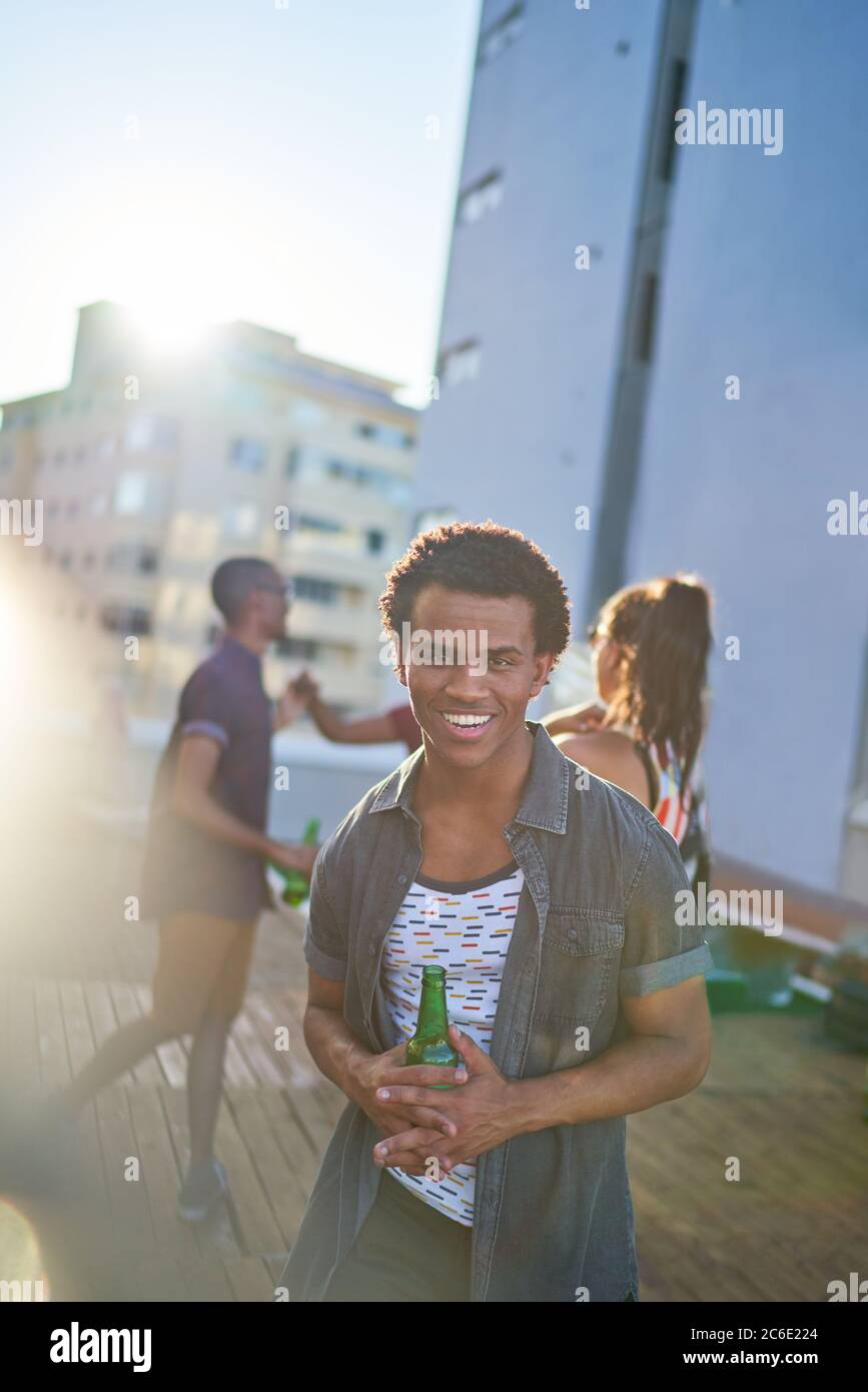 Ritratto felice giovane bevendo birra sul soleggiato tetto urbano Foto Stock