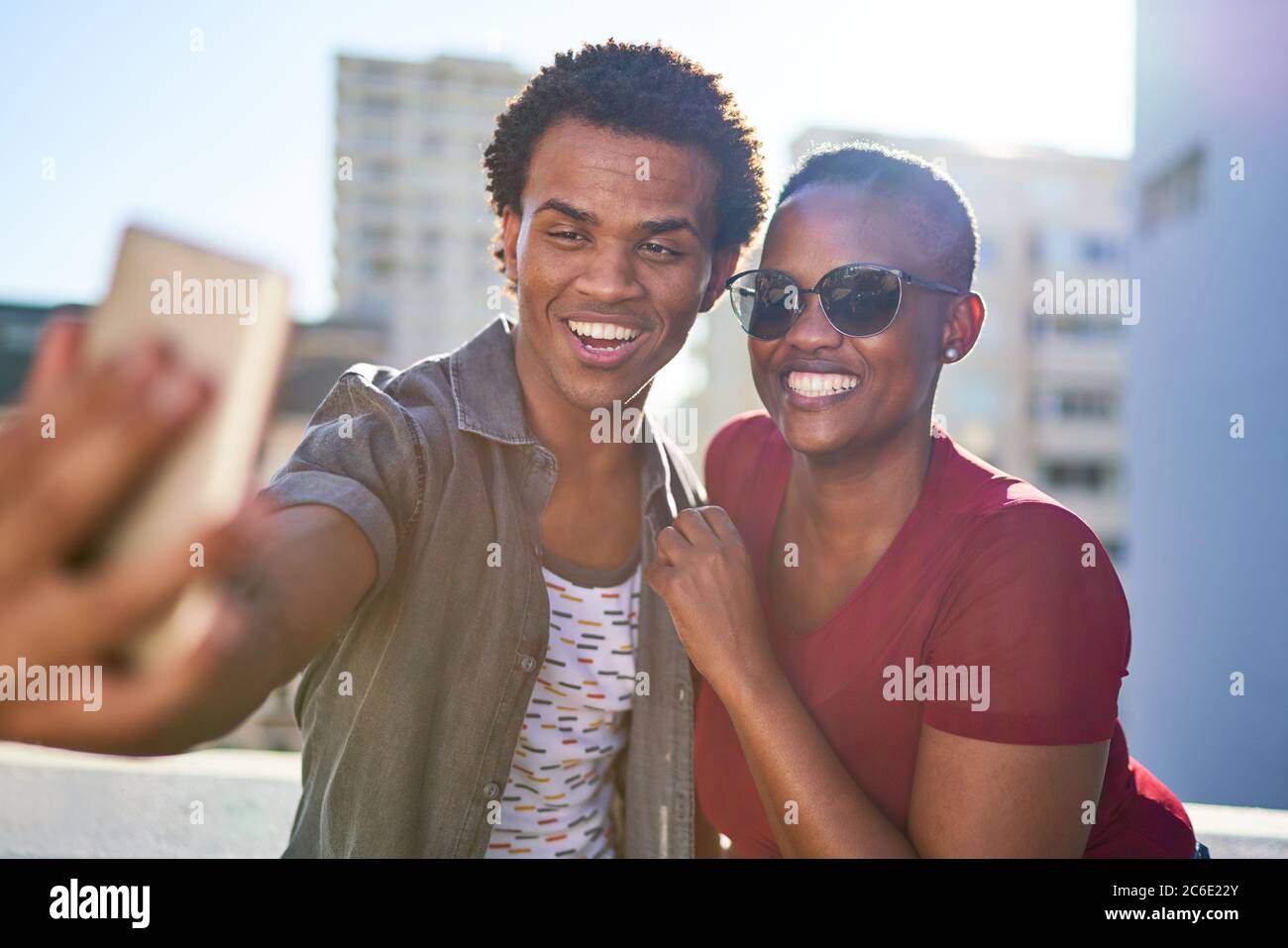 Felice giovane coppia che prende selfie con smartphone sul tetto soleggiato Foto Stock
