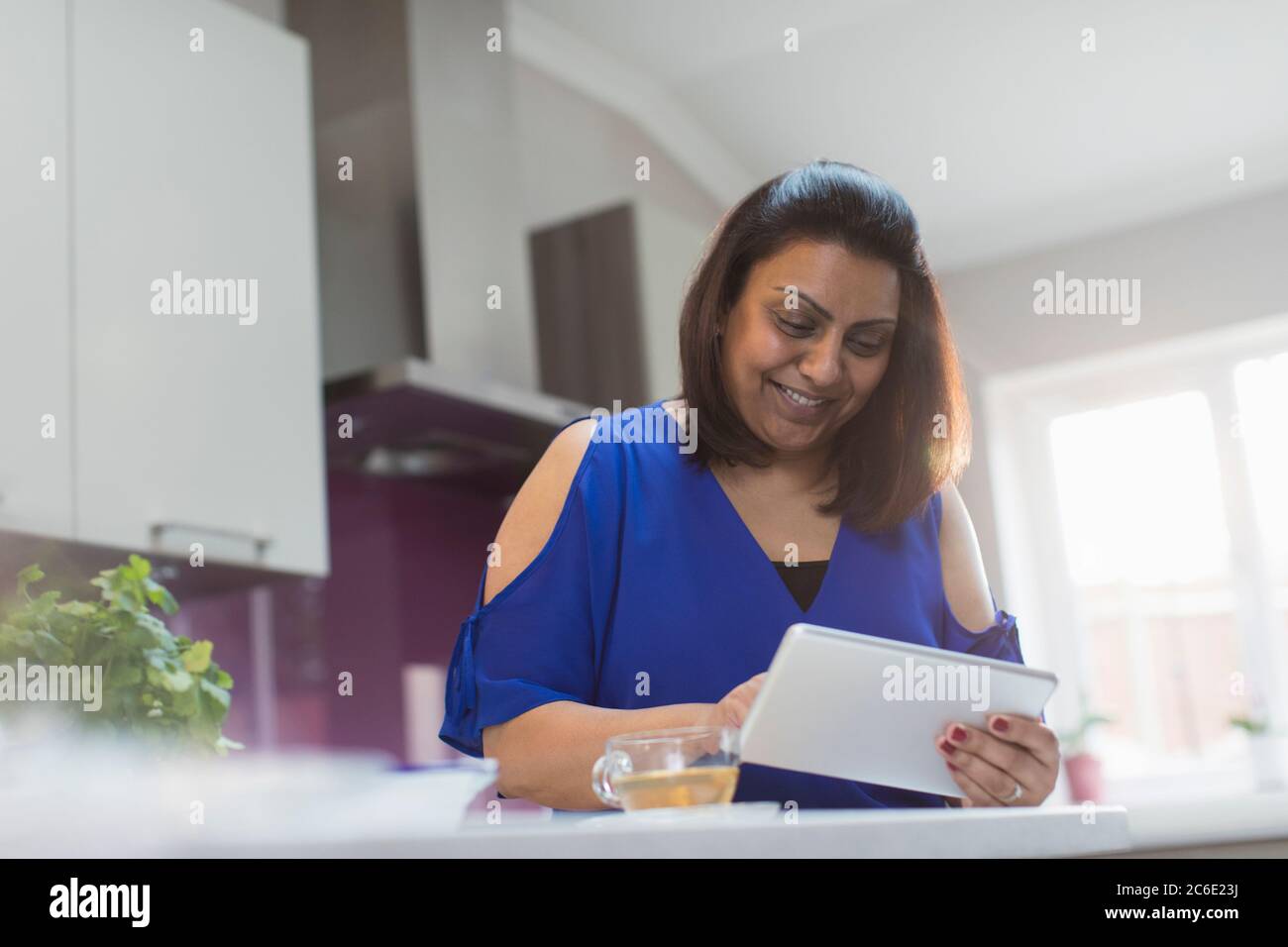 Donna sorridente che usa il tablet digitale in cucina Foto Stock