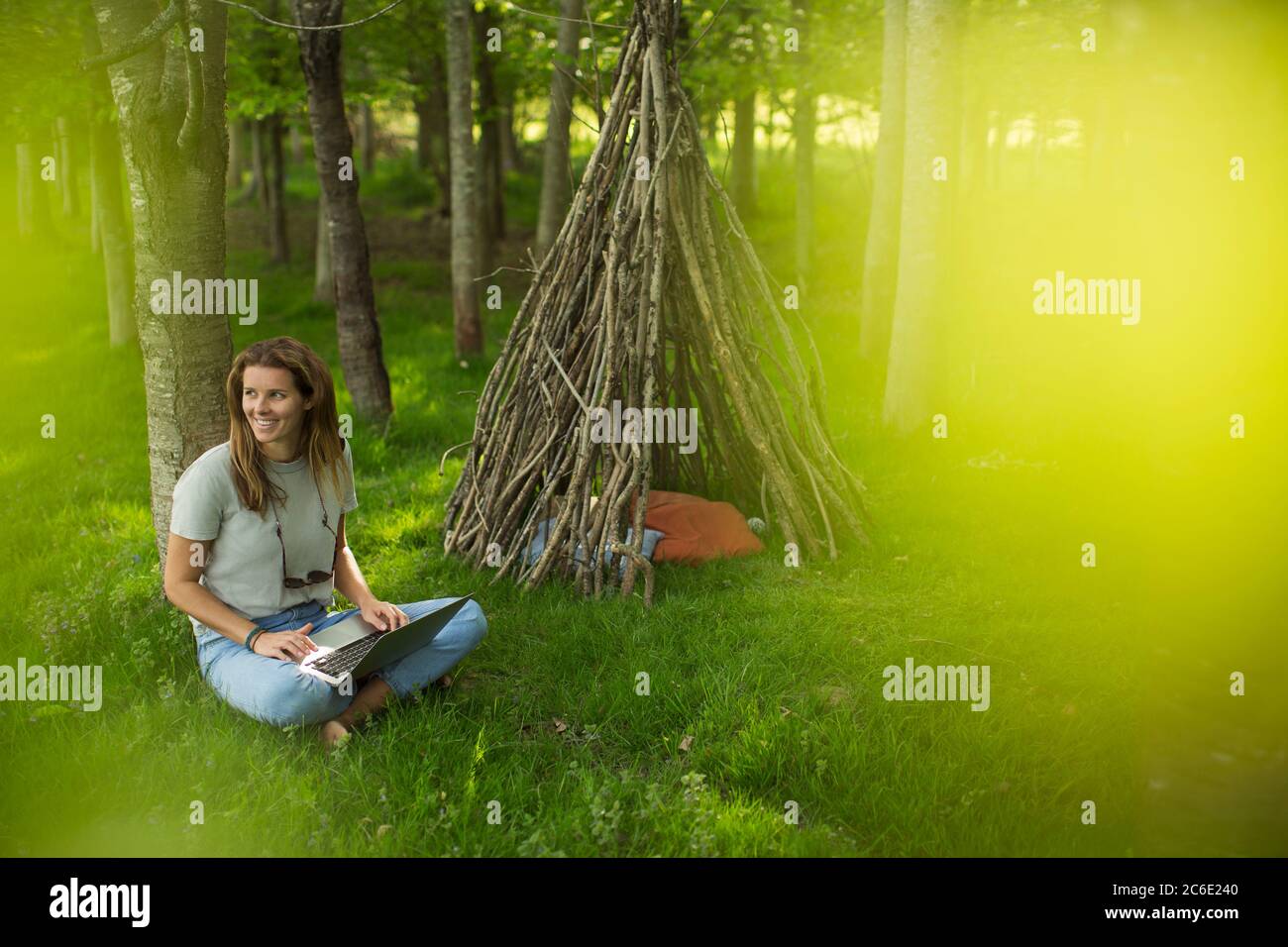 Donna sorridente che usa un laptop fuori dalla branca in legno Foto Stock