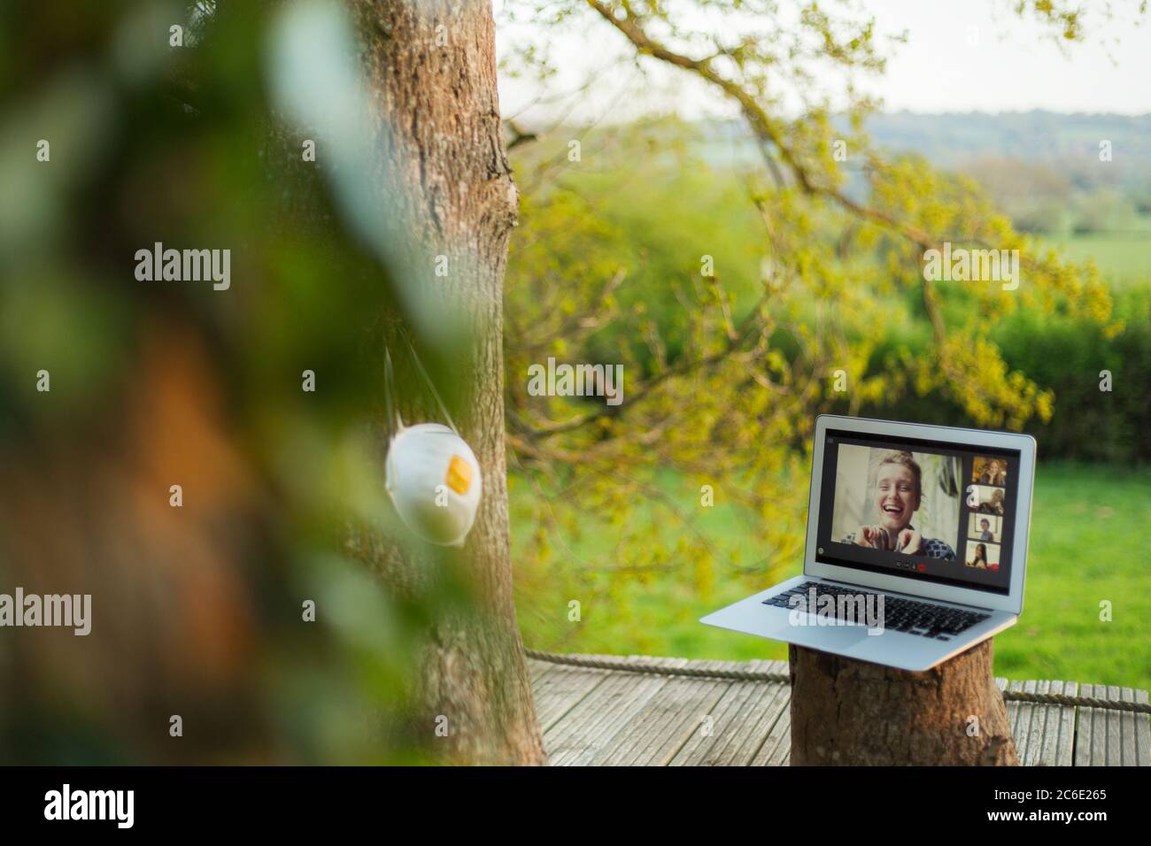 Maschera facciale appesa sull'albero accanto agli amici che chattano video sul laptop Foto Stock