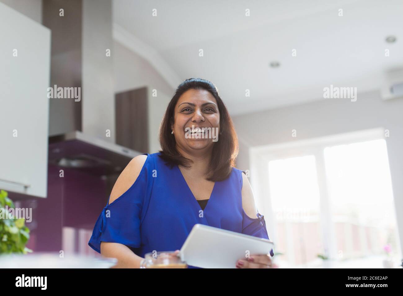 Ritratto donna felice utilizzando tablet digitale in cucina Foto Stock