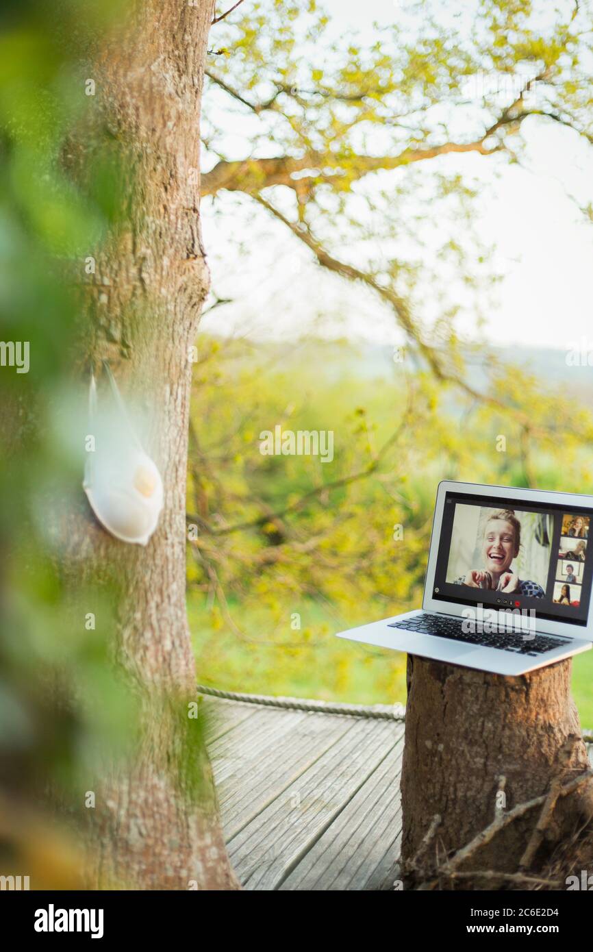 Maschera facciale appesa sull'albero vicino agli amici che chattano video sullo schermo del laptop Foto Stock