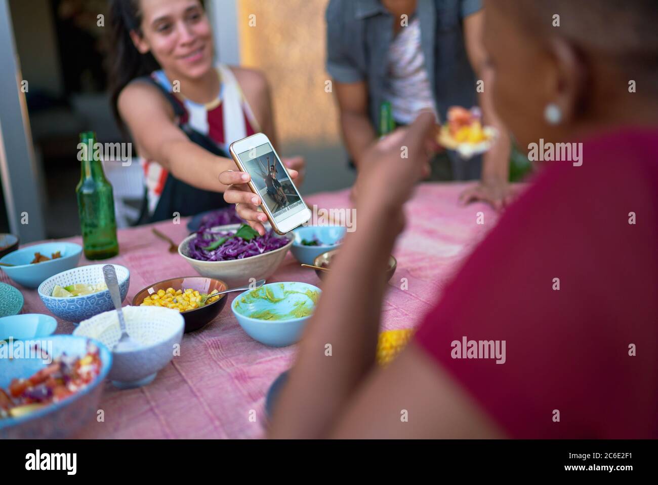 Giovane donna che mostra smartphone ad un amico al tavolo del patio Foto Stock