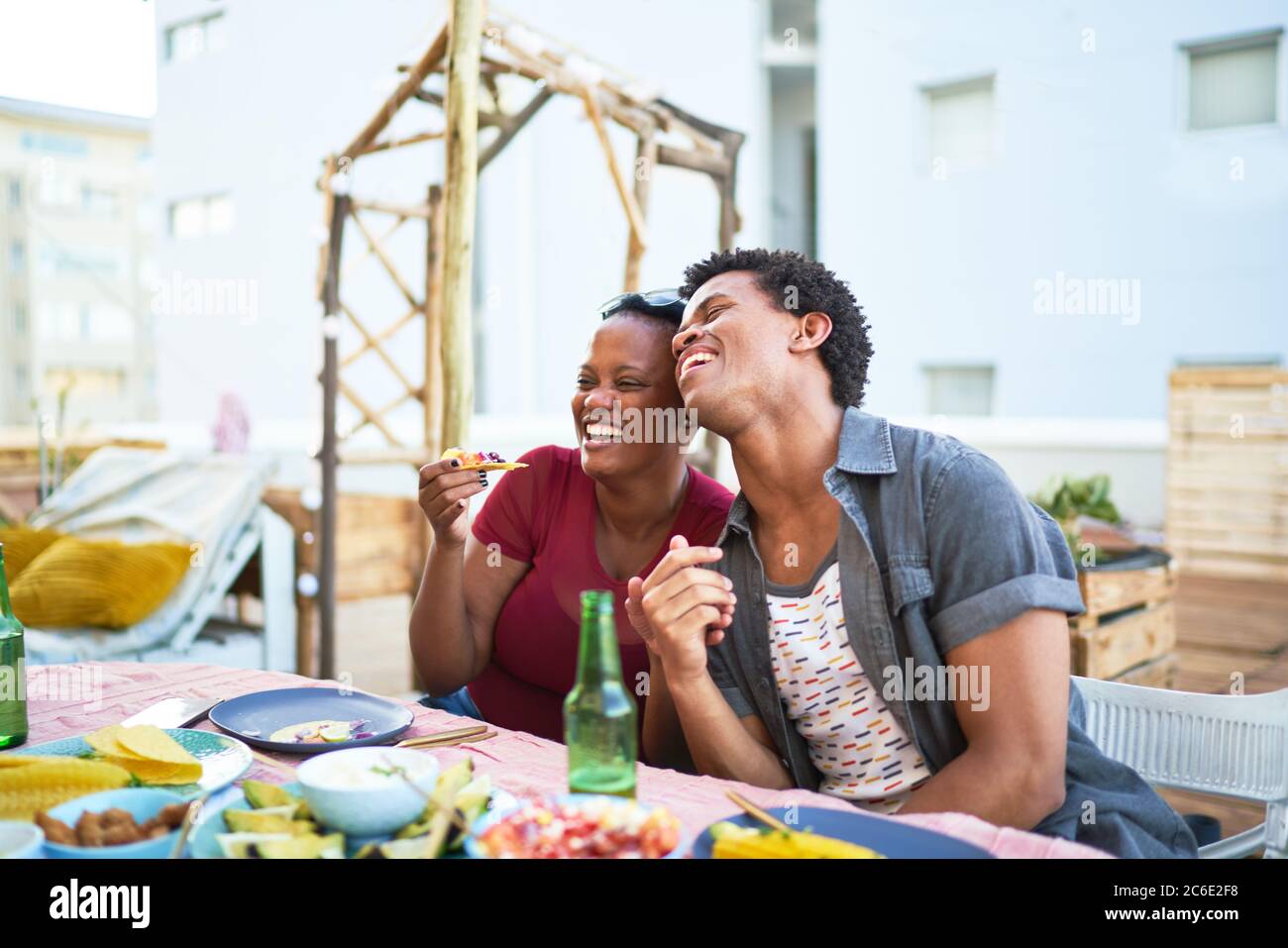 Felice giovane coppia ridendo e mangiando al tavolo del patio Foto Stock