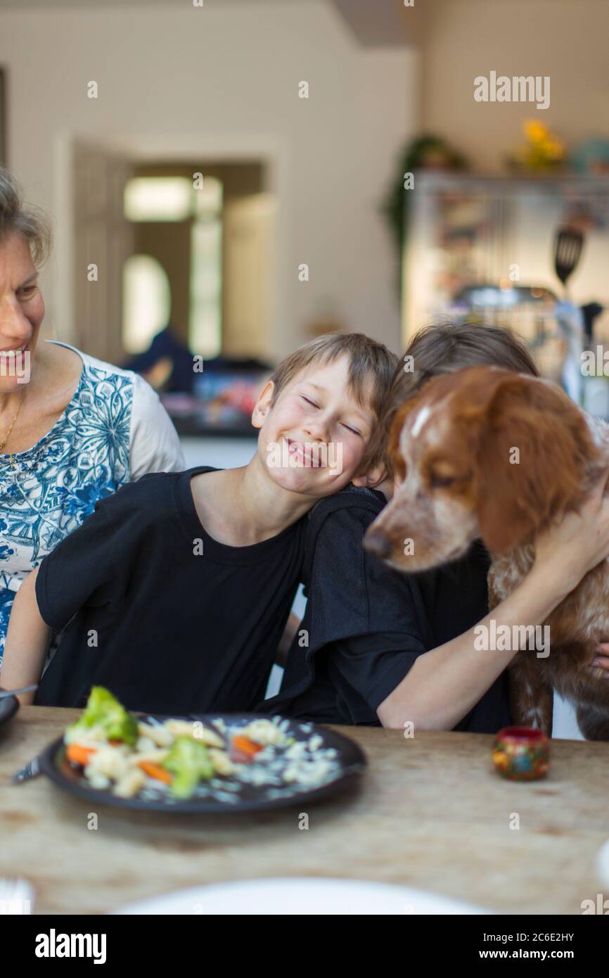 Buona famiglia con il cane che mangia il pranzo al tavolo da pranzo Foto Stock