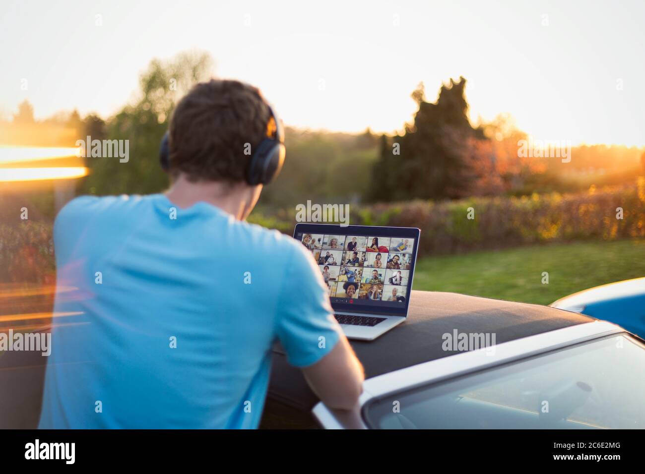 Uomo con cuffie e laptop che parla con gli amici sul tetto dell'auto Foto Stock