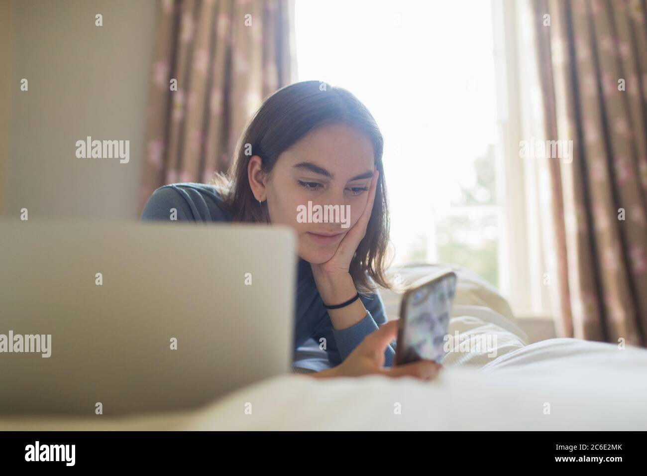 Ragazza adolescente che usa lo smartphone al computer portatile a letto Foto Stock