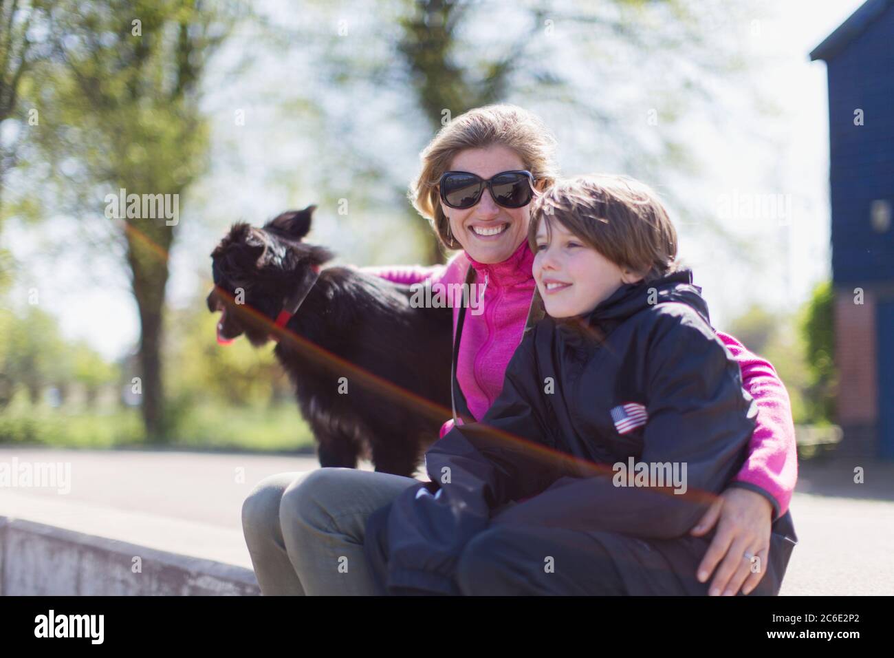 Ritratto felice madre e figlio con il cane sulla sporgenza soleggiata Foto Stock