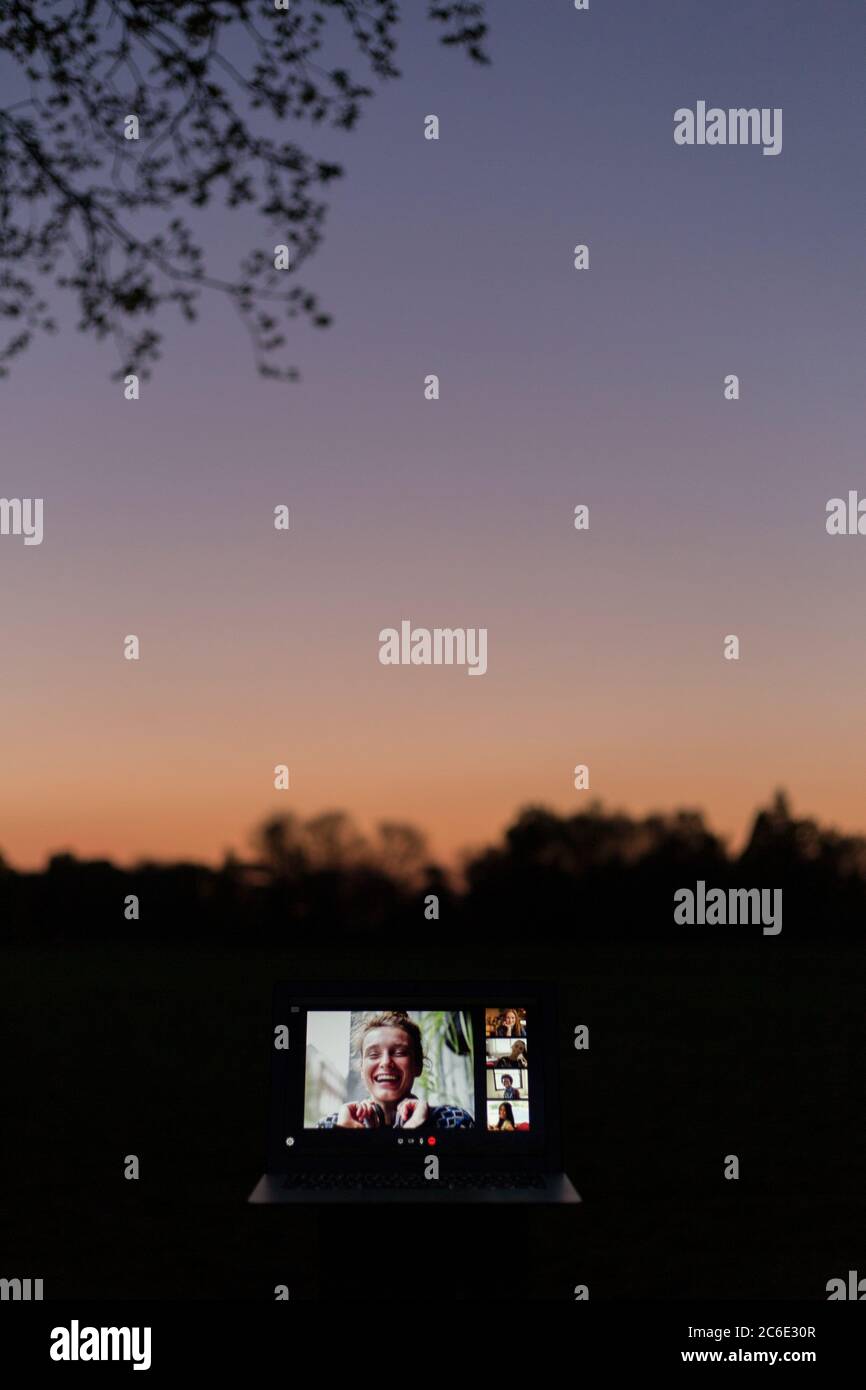 Amici che videochattano sullo schermo del computer portatile in giardino al tramonto Foto Stock