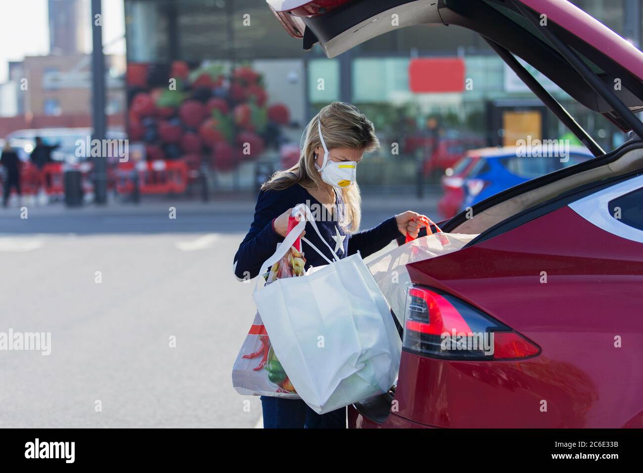 Donna con maschera facciale che carica gli alimentari in auto nel parcheggio Foto Stock