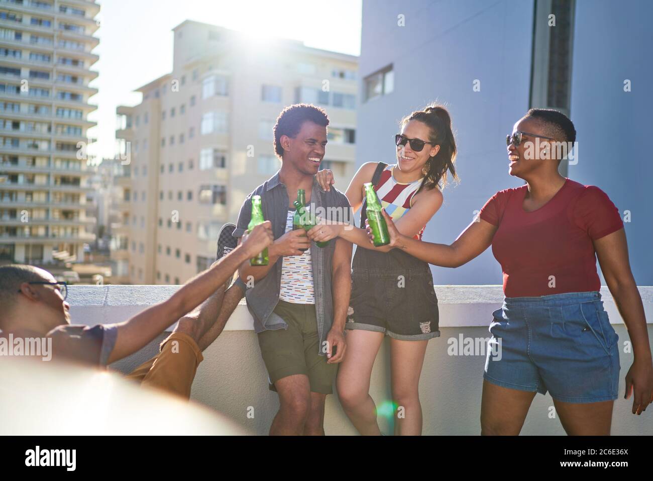 Felici i giovani amici che tostano le bottiglie di birra sul luminoso balcone urbano Foto Stock