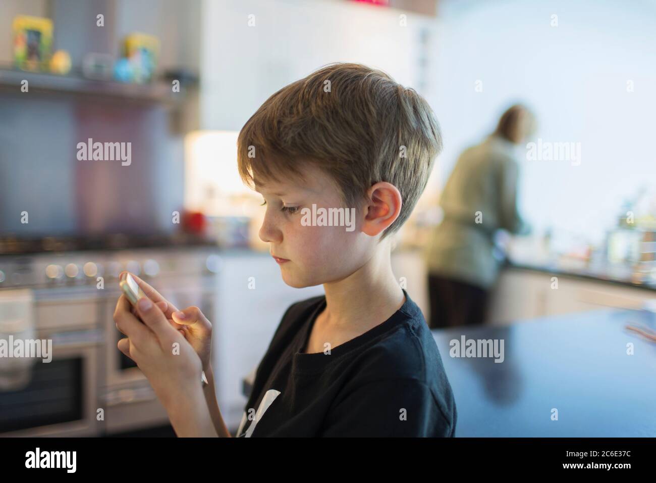 Ragazzo che usa lo smartphone in cucina Foto Stock