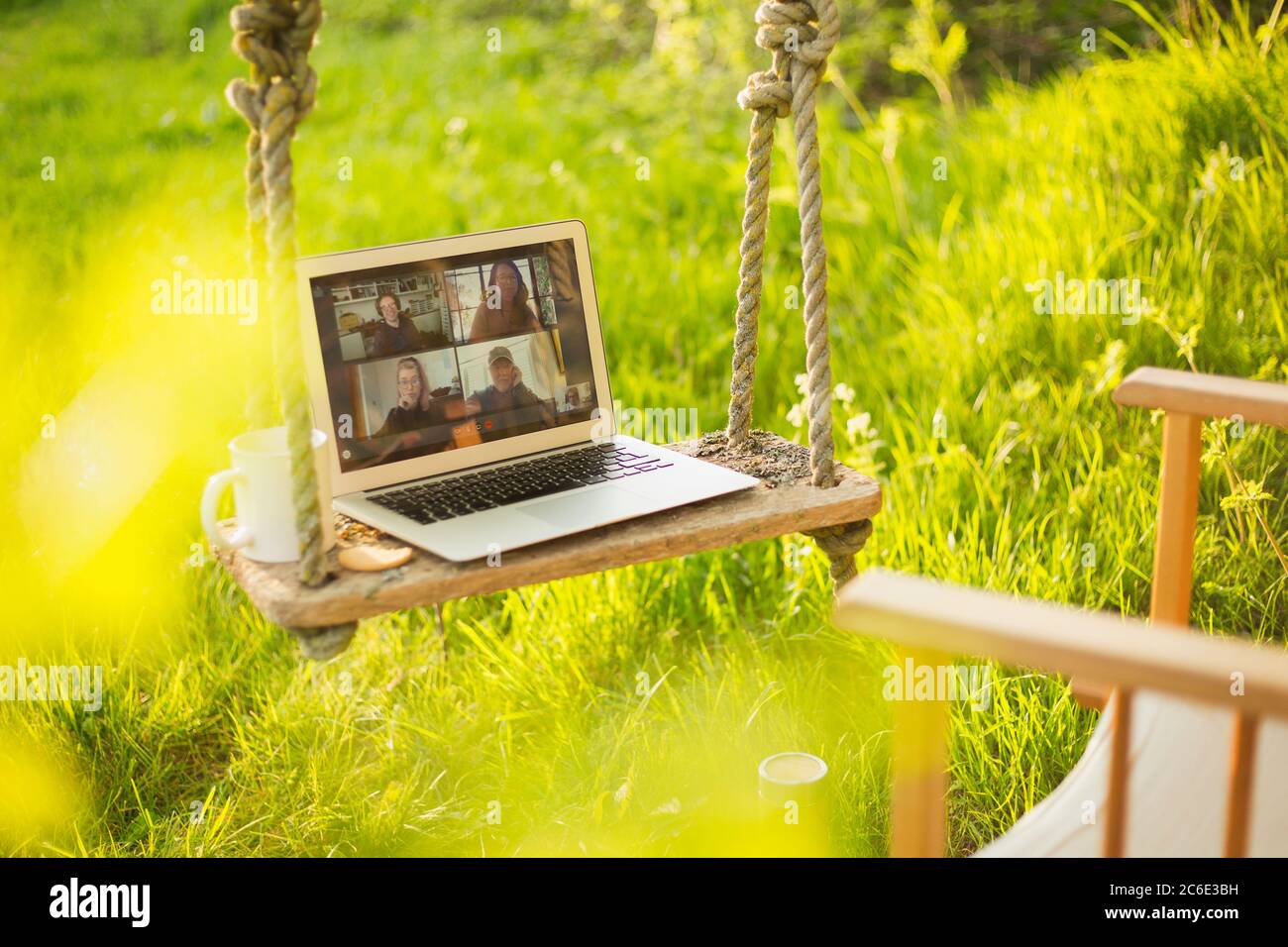 I colleghi videochattano sullo schermo del laptop su un'oscillazione rustica in giardino Foto Stock