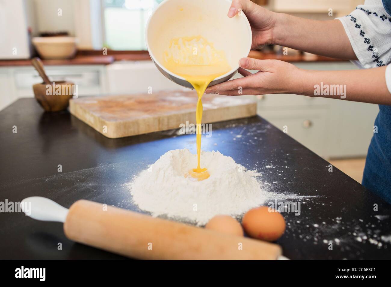 Ragazza adolescente che versa tuorli d'uovo nel nido di farina sul banco della cucina Foto Stock