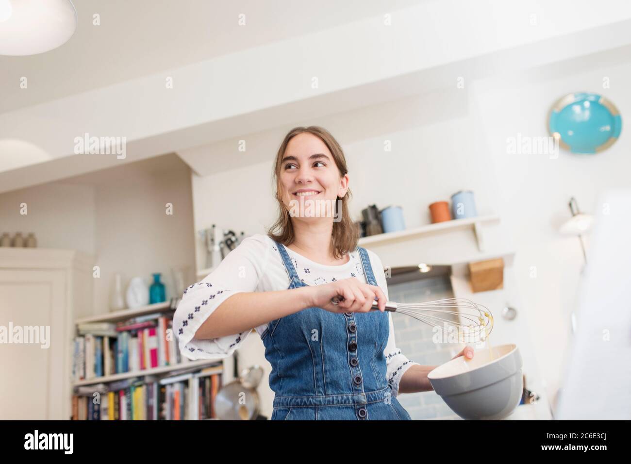 Sorridente ragazza adolescente con frusta e ciotola cottura in cucina Foto Stock