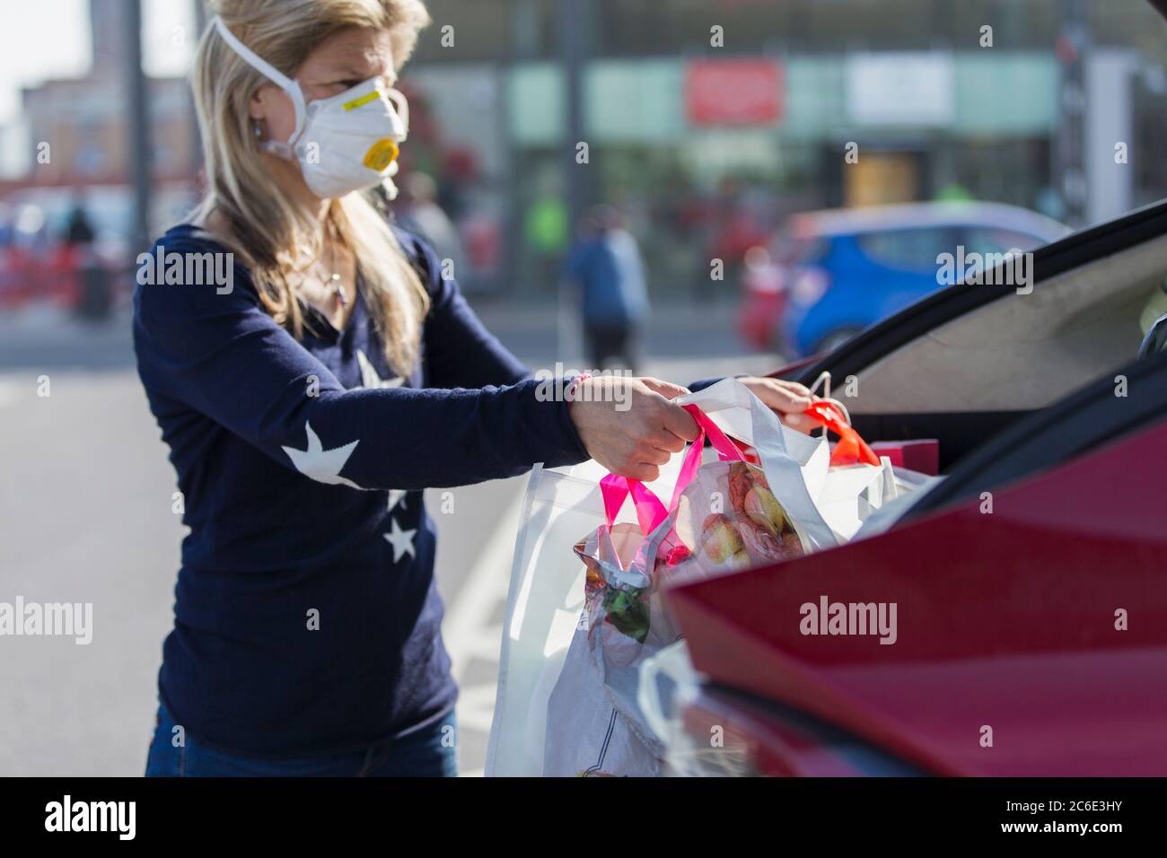 Donna in maschera di faccia caricando gli alimentari in auto Foto Stock