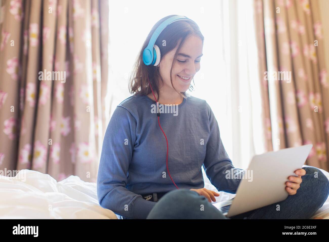 Ragazza adolescente con cuffie e computer portatile che chattano video a letto Foto Stock