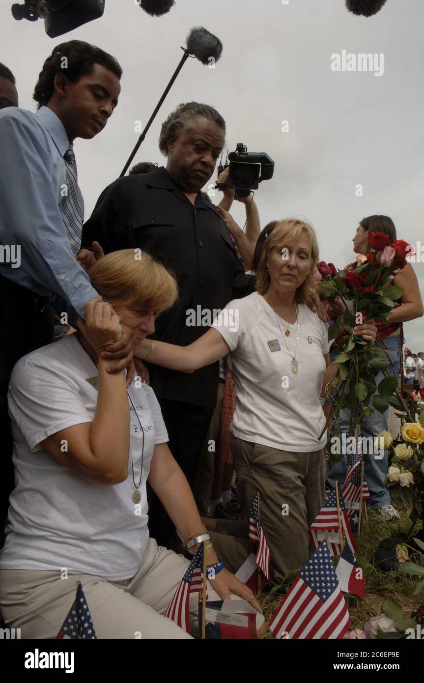 Crawford, Texas 28 agosto 2005: L'attivista anti-guerra Cindy Sheehan (a sinistra) e Jane Bright (a destra) si inginocchiano davanti a una mostra di croci come il Rev. Al Sharpton di New York (in nero) guarda a Camp Casey II vicino al ranch del presidente degli Stati Uniti George W. Bush ©Bob Daemmrich Foto Stock
