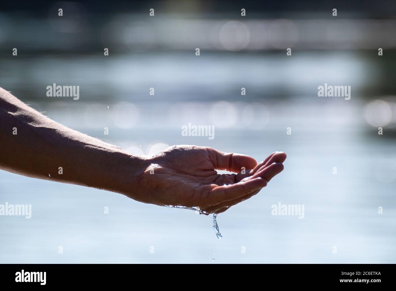 Mano con acqua. Afferrare acqua pura in gocce di mano che cadono nella superficie dell'acqua con fondo bokeh Foto Stock Mano con acqua. Afferrare acqua pura in gocce di mano che cadono nella superficie dell'acqua con fondo bokeh Foto Stock