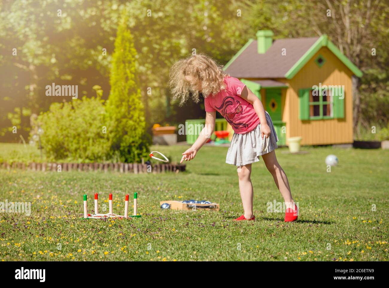 Carino bambina di 6 anni giocare corda PEG tiro gioco in giardino casa all'aperto nella soleggiata giornata estiva. Concetto di attività per il tempo libero. Foto Stock