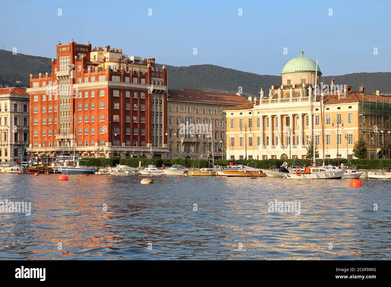 Ora d'oro sul lungomare di Trieste, Italia con 2 palazzi signorili e belli: Palazzo Aedes (in rosso) e Palazzo Carciotti. Foto Stock