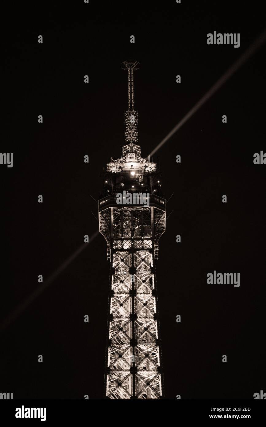 Primo piano della punta della Torre Eiffel di notte con la luce del suo riflettore che illumina il cielo Foto Stock