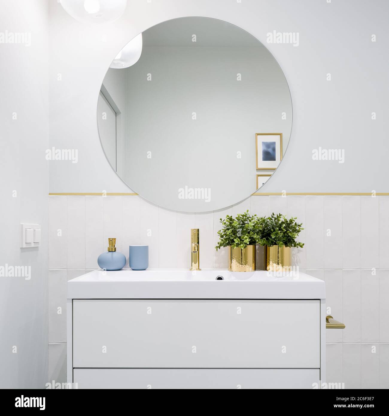 Bagno luminoso con specchio rotondo, armadio bianco con cassetti e decorazioni blu e dorate Foto Stock