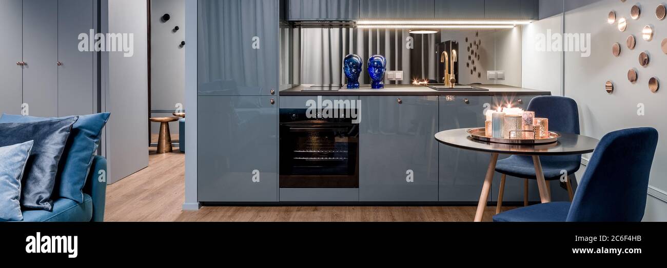 Panorama di interni di cucina affascinante in blu con elegante zona pranzo e decorazioni dorate Foto Stock