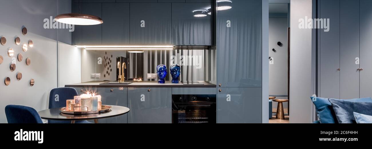 Panorama di interni blu scuro con cucina a vista e zona pranzo con tavolo rotondo Foto Stock